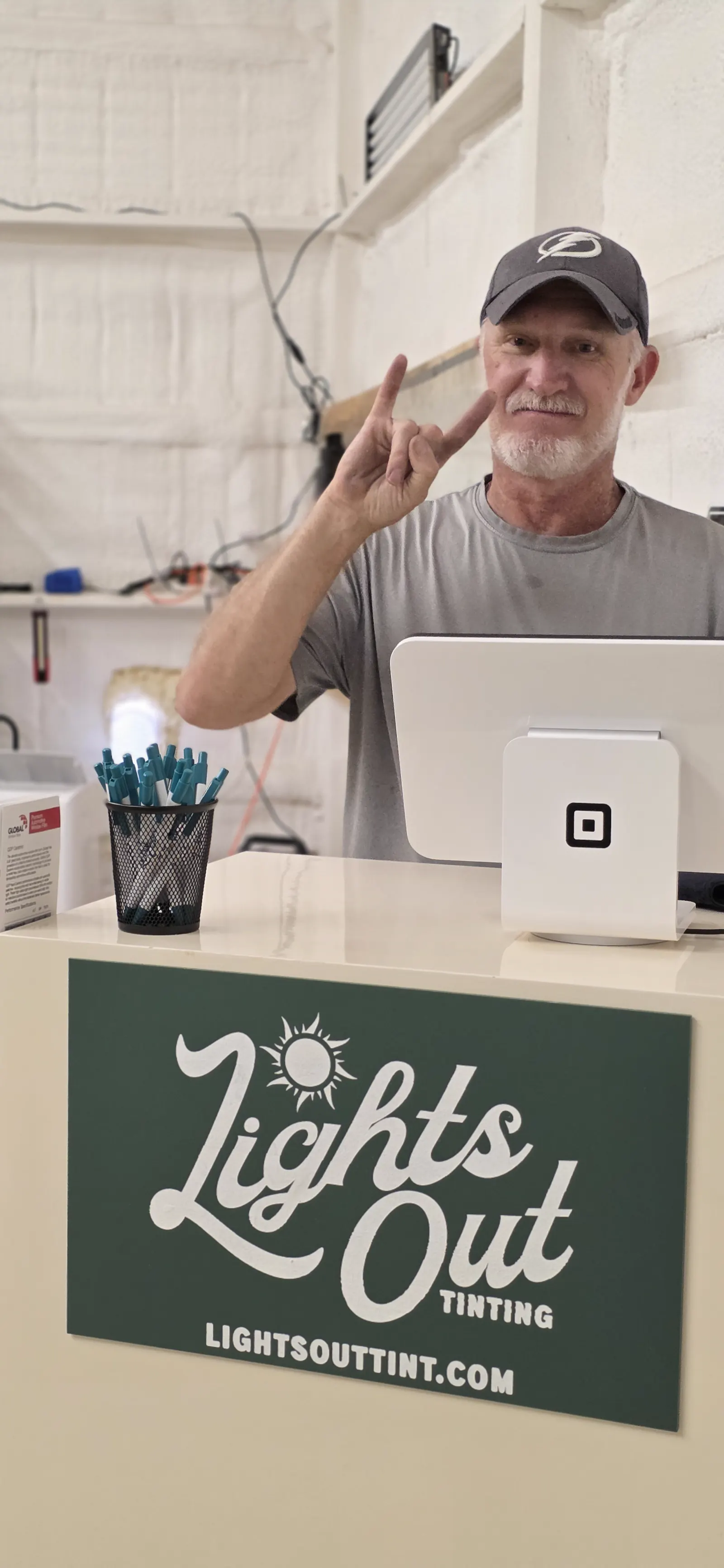 Robert, owner of Lights Out Tinting, in his Freeport shop, smiling and giving a peace sign
