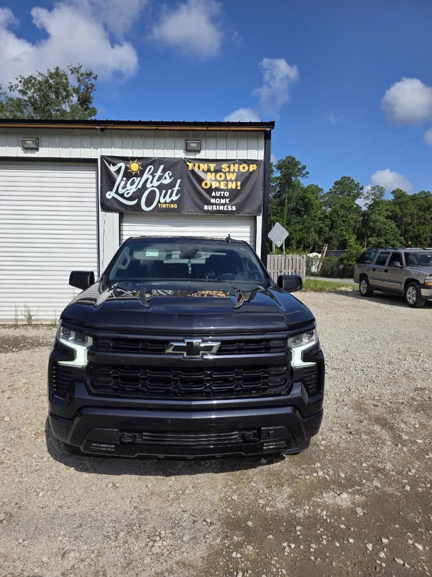 A black full-size pickup with freshly tinted windows in front of the hand-painted Lights Out Tinting sign.