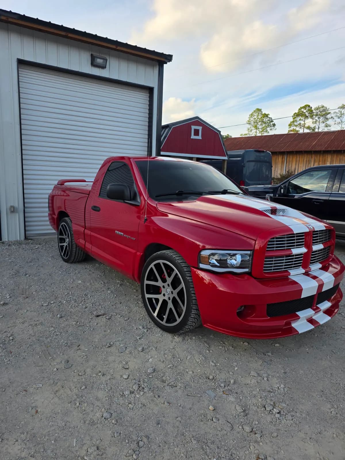 A red pickup with racing stripes and freshly tinted windows beside the red barn shop.