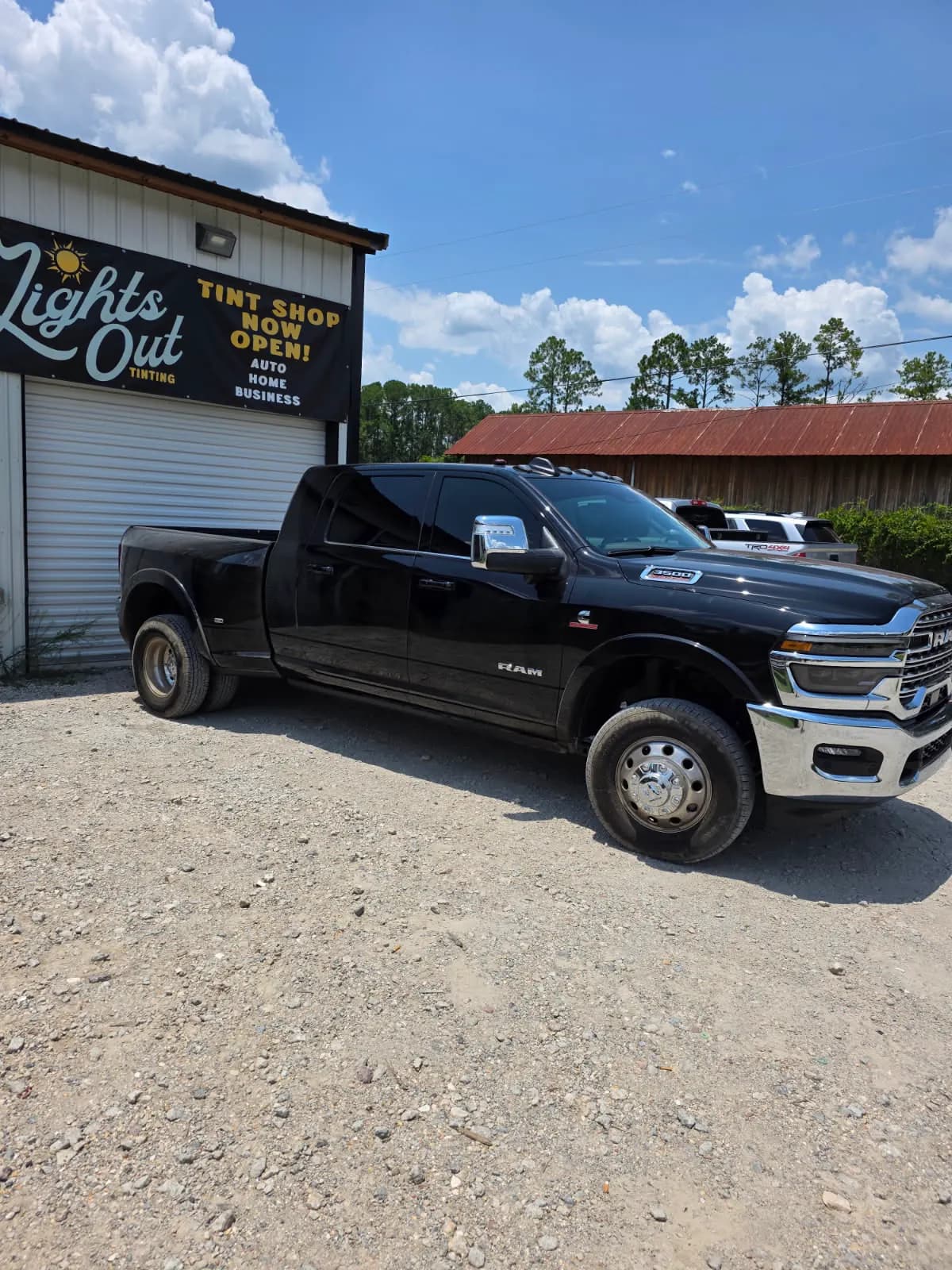 A black Ram dually pickup with tinted windows in front of the Lights Out Tinting sign.