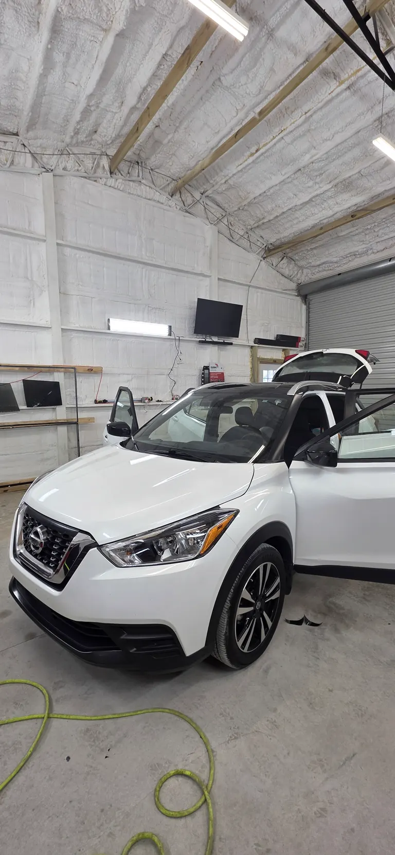 White Nissan Kicks in the shop bay with the doors open, mid tint job