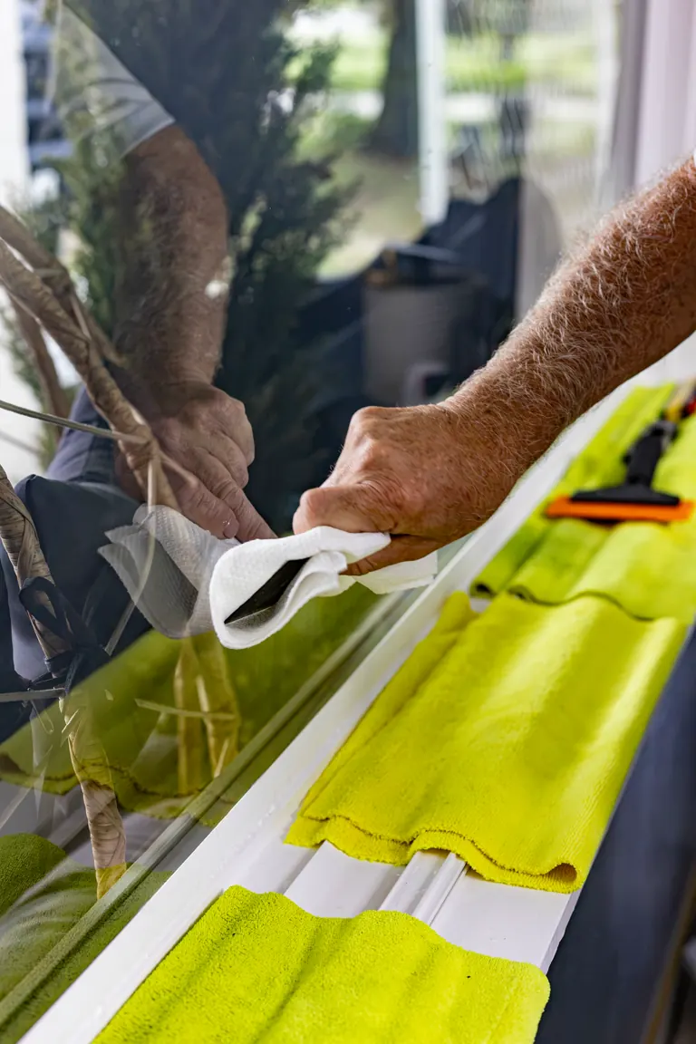 Wiping the edge of a newly filmed house window clean, microfiber towels laid out along the sill